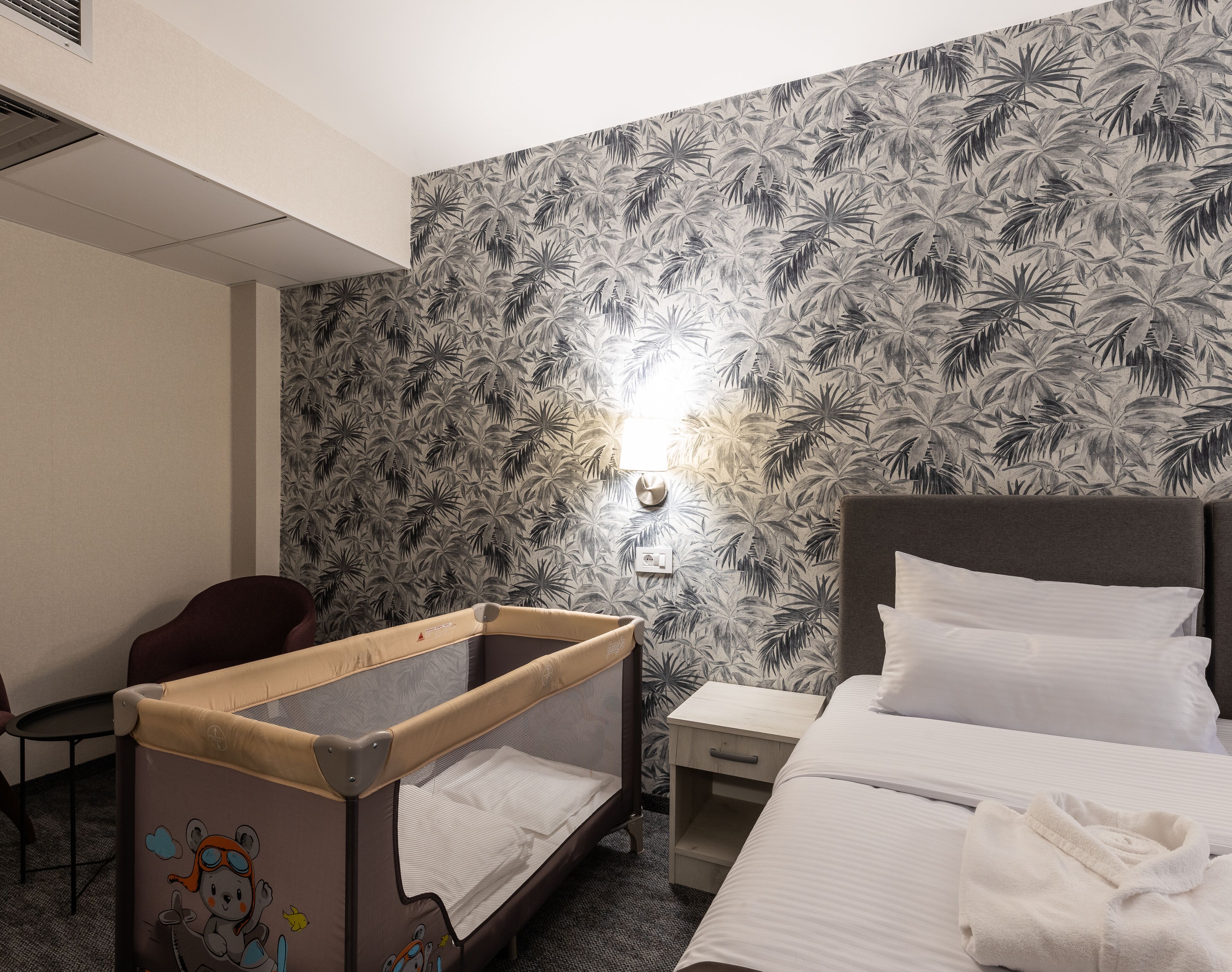A hotel room with a bed, a small desk, a chair, and a crib with a cartoon character.