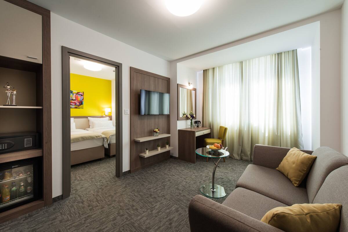 A hotel room with a bed, a sofa, a TV, a desk, and a glass coffee table.