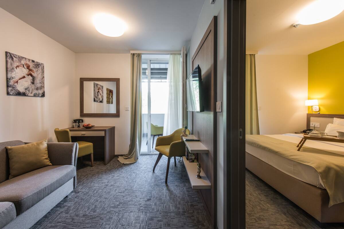 A hotel room with a sofa, a desk, a bed, and a television.