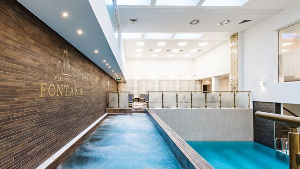 A spa area with a large indoor pool, a brick wall with the name 'FONTANA', and a ceiling with recessed lighting. - Hotel Fontana (Vrnjacka Banja)