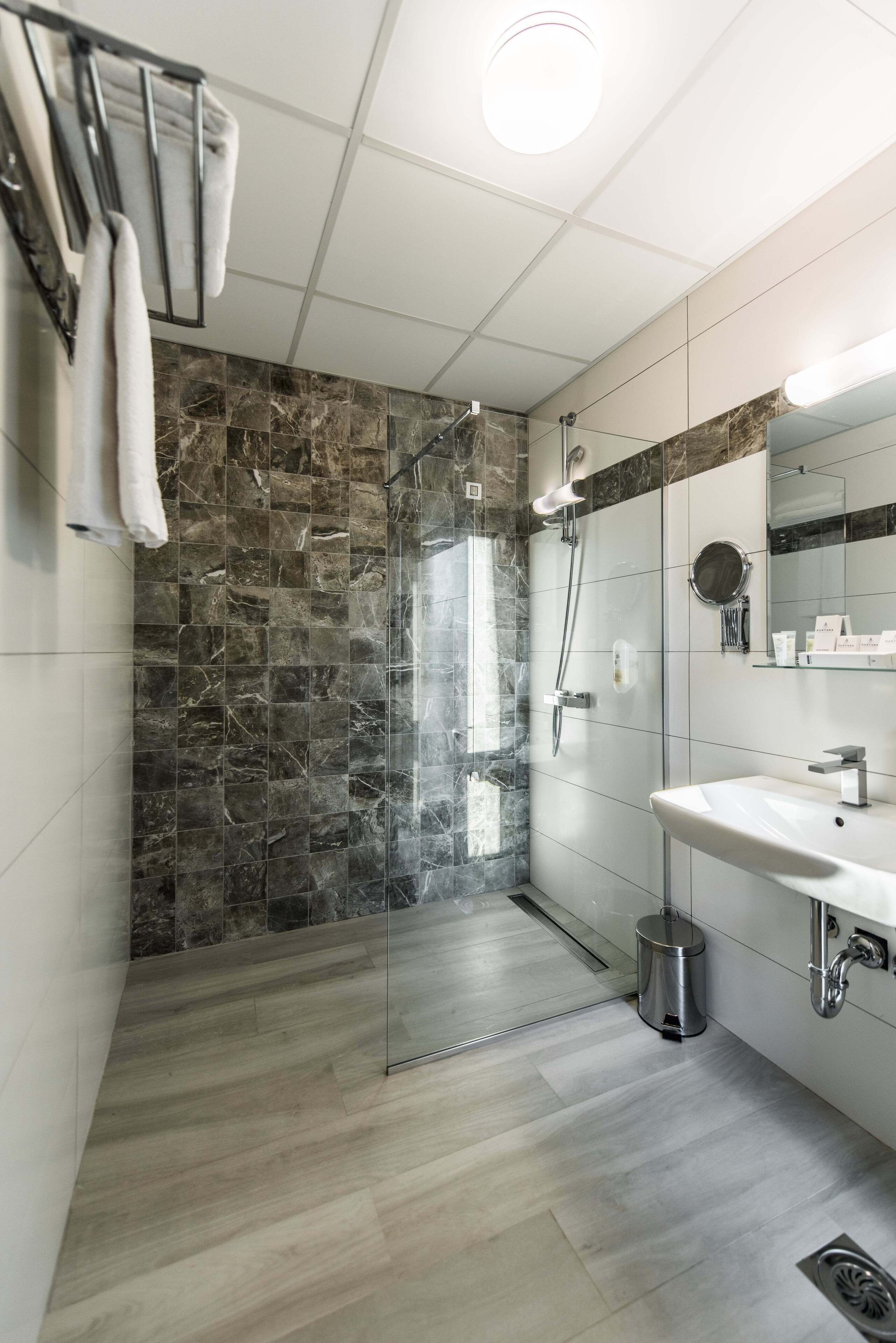 A modern bathroom with a glass-enclosed shower, a white sink, and a marble-tiled wall.