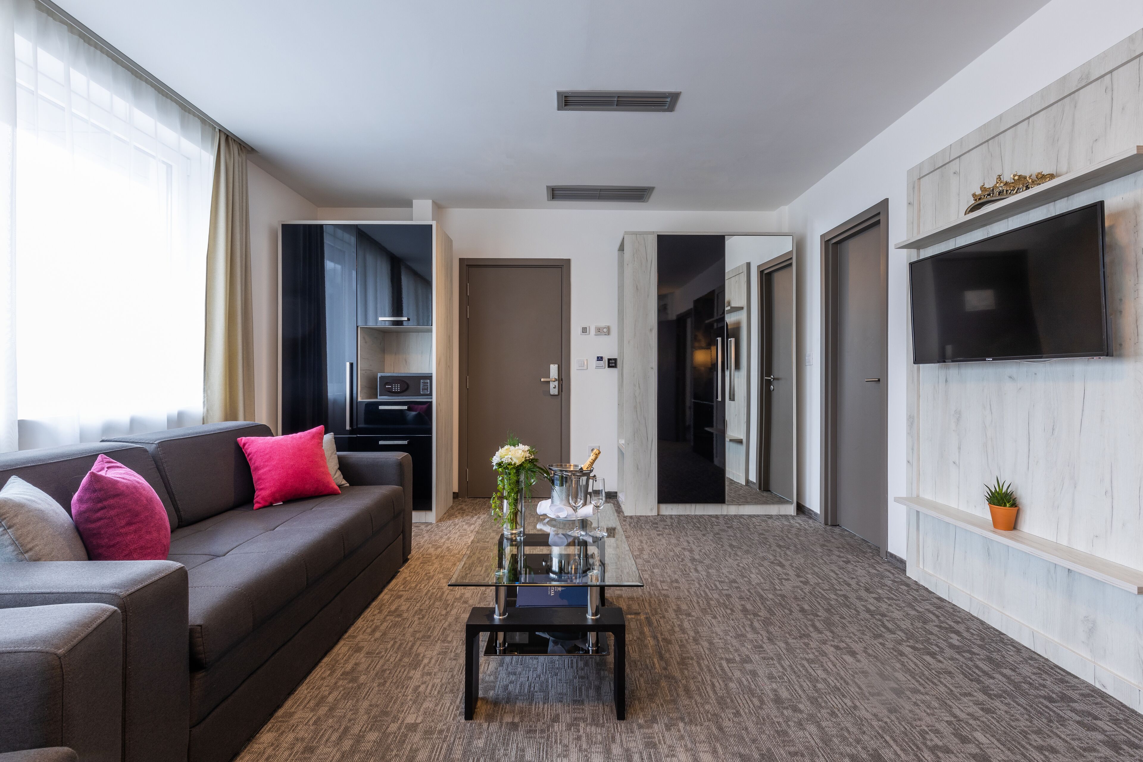 Un moderno salón con un sofá, una mesa de centro de vidrio y un televisor montado en la pared.