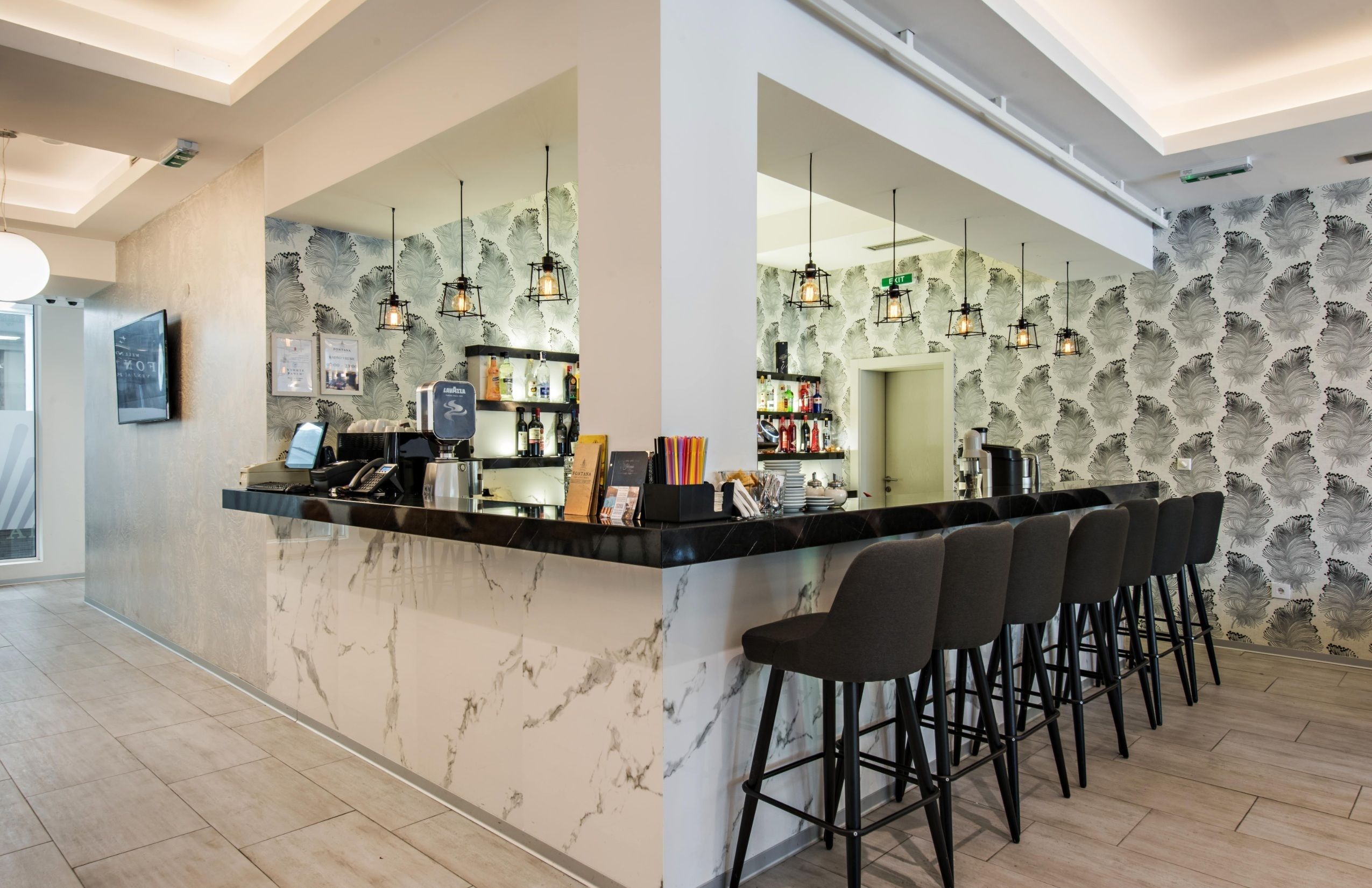 Un espace bar moderne doté d’un comptoir en marbre, de tabourets de bar noirs et de luminaires suspendus.