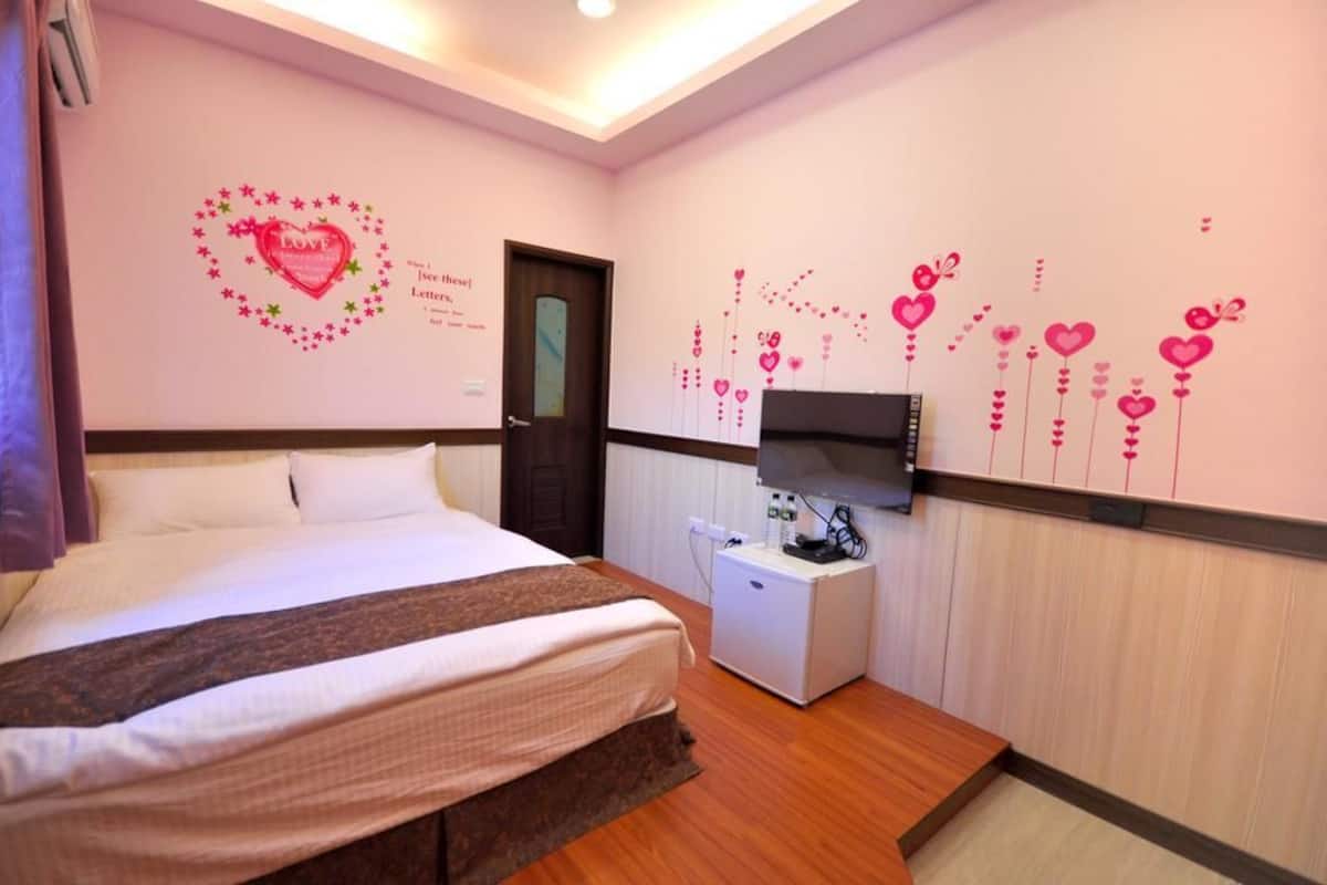 A hotel room with a bed, a TV on a small table, and decorative heart decals on the walls.