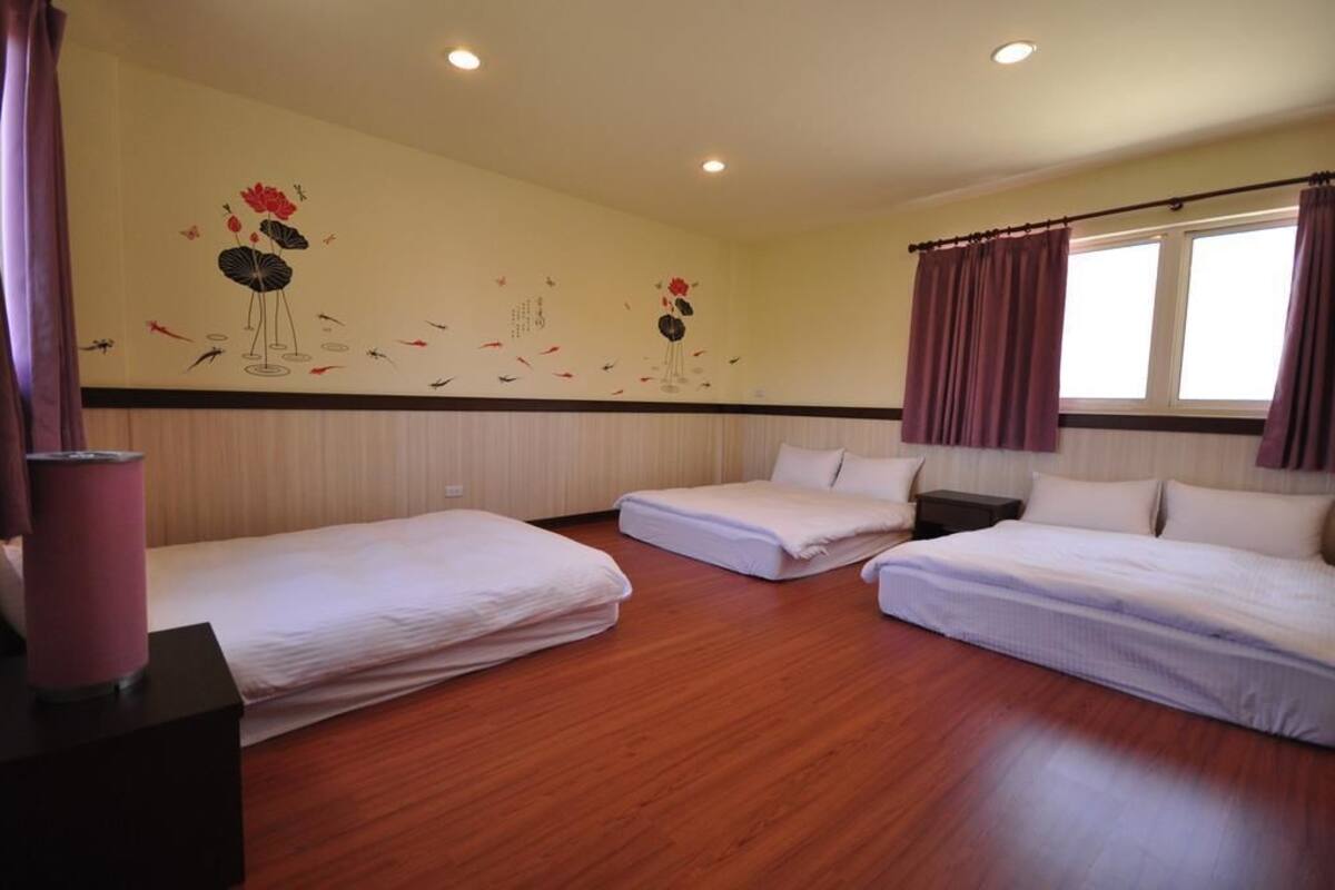 A hotel room with two beds, a wooden floor, and a wall mural with floral and bird designs.