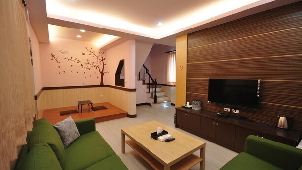 A modern living room with green sofas, a wooden coffee table, a flat-screen TV, and a staircase in the background. - Seasons B&B (Liuqiu)