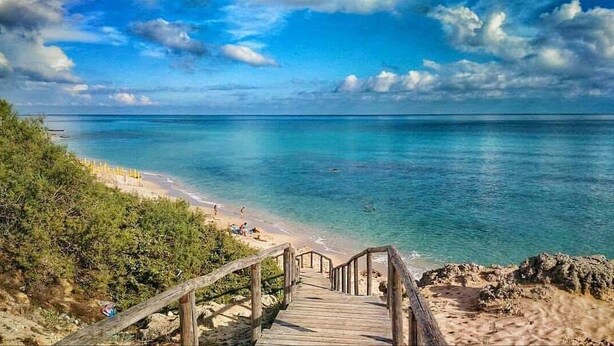A wooden staircase leading to a beach with clear turquoise water and a wooden railing.