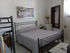 Un dormitori amb un llit individual, un llit superposat, una taula petita amb un ram i un mirall a la paret.