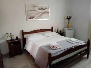 Un llit ben fet amb roba de llenceria blanca, una taula de nit amb una làmpada i un petit objecte decoratiu.
