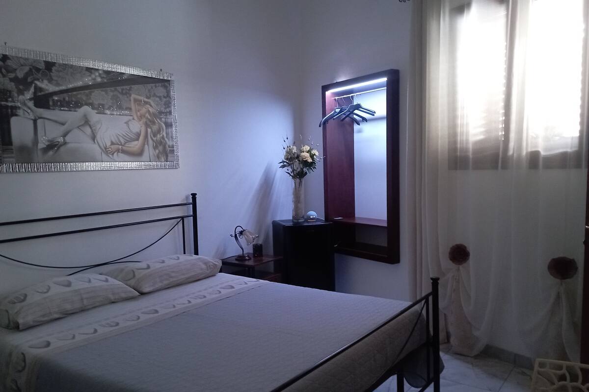 Une chambre à coucher comprenant un lit, une table de chevet, un miroir et une étagère fixée au mur.
