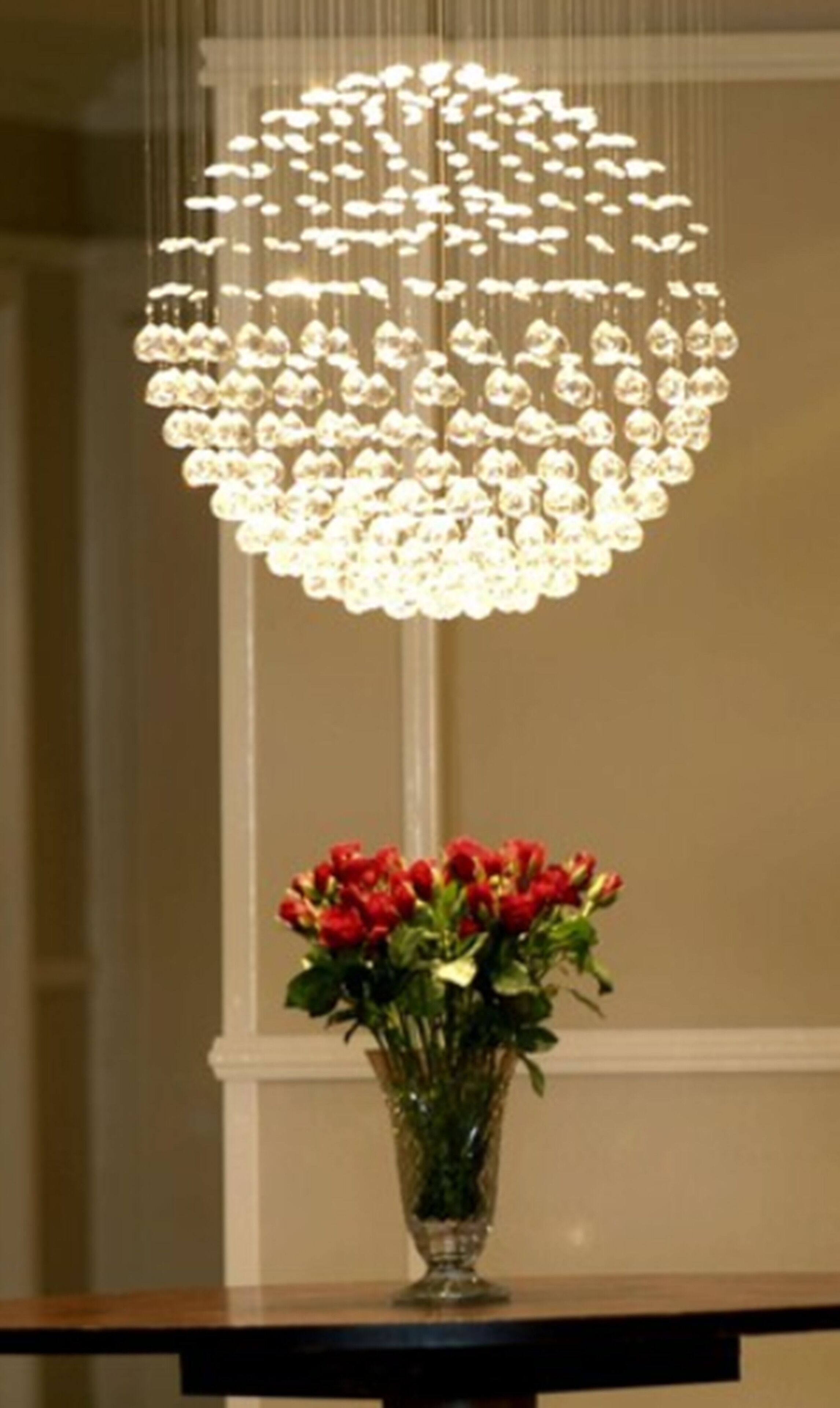 A chandelier with multiple bulbs and a vase of red flowers on a table.