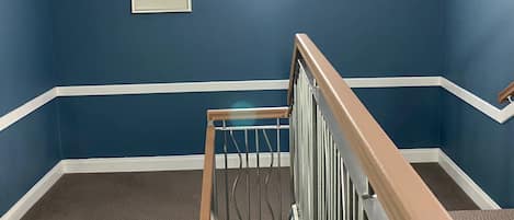 A staircase with a wooden handrail leading to a landing. The walls are painted blue with white trim.