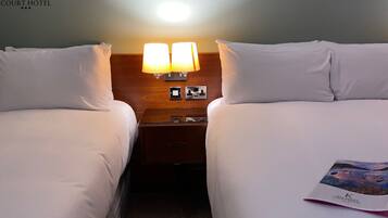 Una habitación de hotel con dos camas, una mesita de noche con lámparas y un folleto de bienvenida sobre la cama.