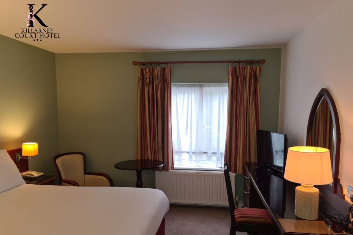 A hotel room with a bed, a desk with a lamp, a chair, a television, and a window with curtains.