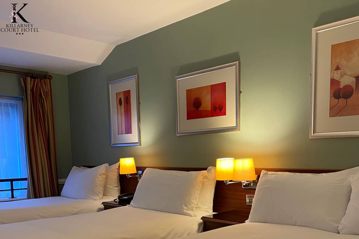A hotel room with two beds, a window with curtains, and two wall-mounted lamps.
