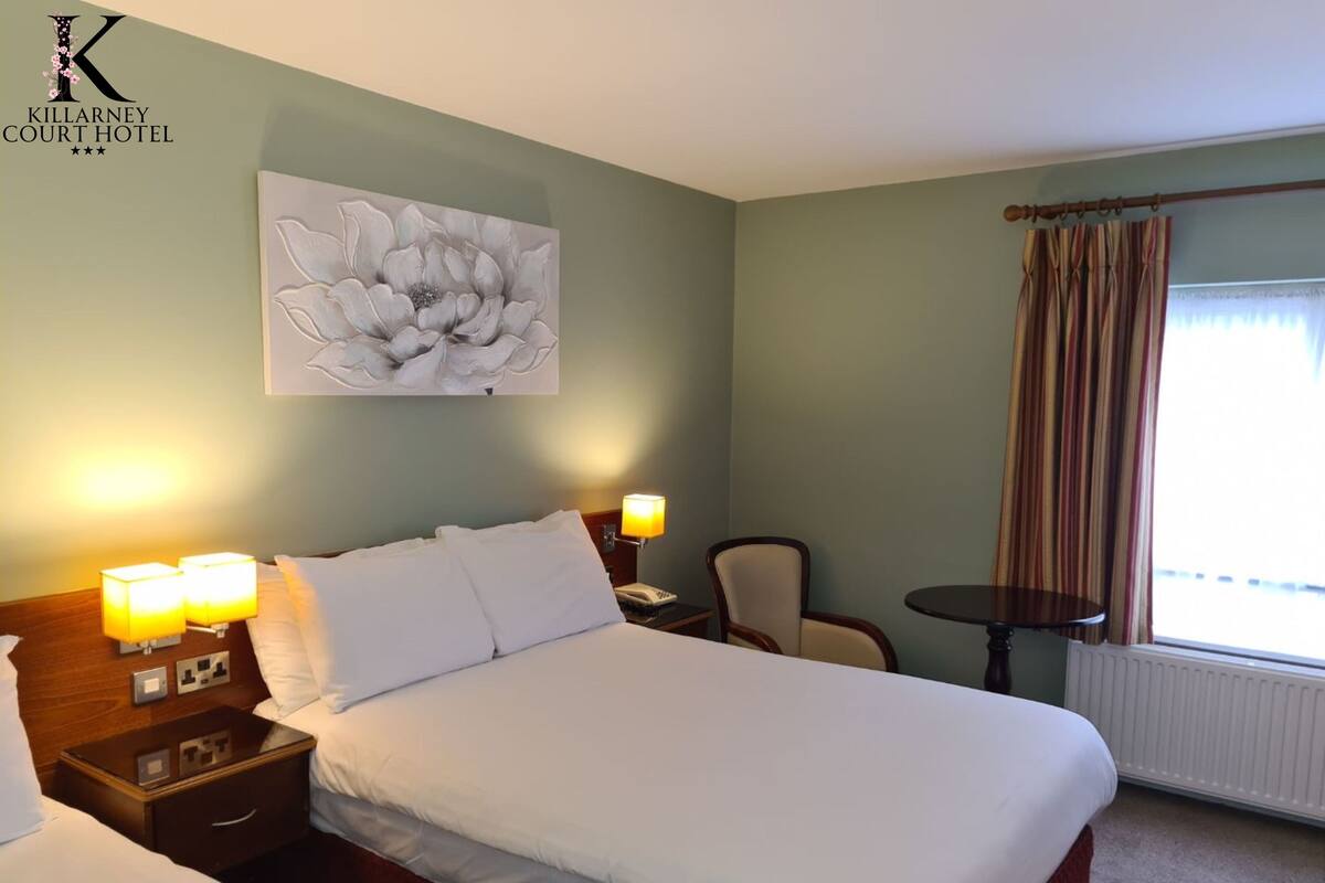 A hotel room with a large bed, bedside lamps, a chair, a small table, and a window with curtains.