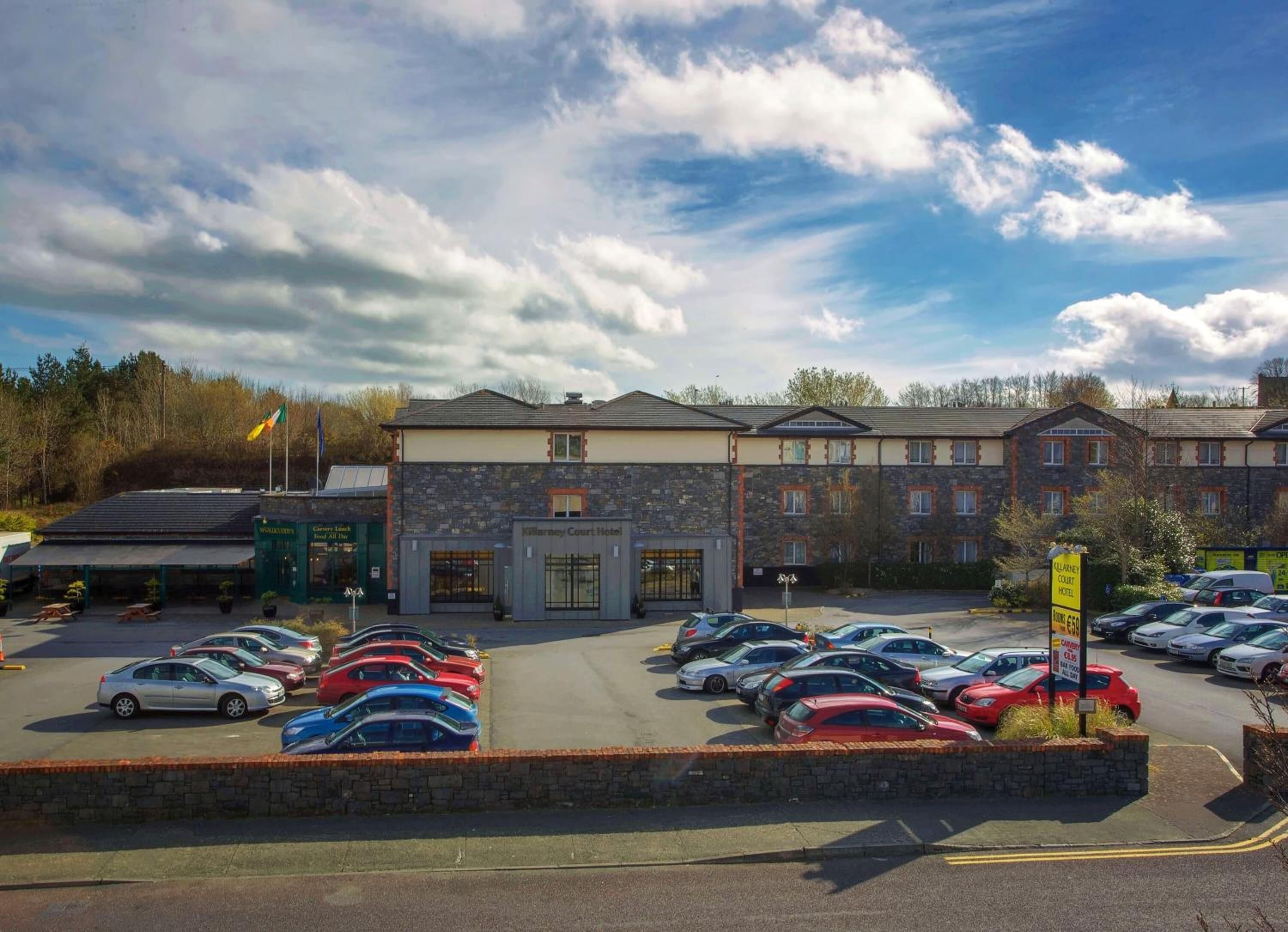 A hotel with a parking lot filled with cars, a stone facade, and a sign indicating the hotel name.