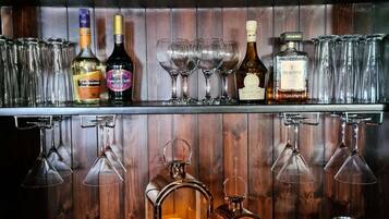 Zona de bar con estantes llenos de botellas de licor, vasos y dos faroles encendidos.