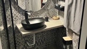 Un baño pequeño con un espejo redondo, un lavabo negro, un inodoro y baldosas estampadas.