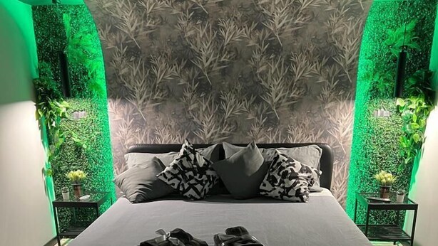 Un dormitorio moderno con una cama grande, iluminación ambiental verde y una pared con estampado de bambú.