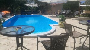 Una piscina con sillones de descanso y sombrillas, rodeada de macetas con plantas y un patio con baldosas.