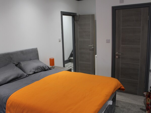 A bedroom with a bed, a nightstand, a mirror, and a door. - Townhouse @ 282 Walthall Street Crewe (Crewe)