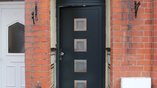 A black door with four square windows, flanked by red brick walls and a white door to the left. - Townhouse @ 282 Walthall Street Crewe (Crewe)