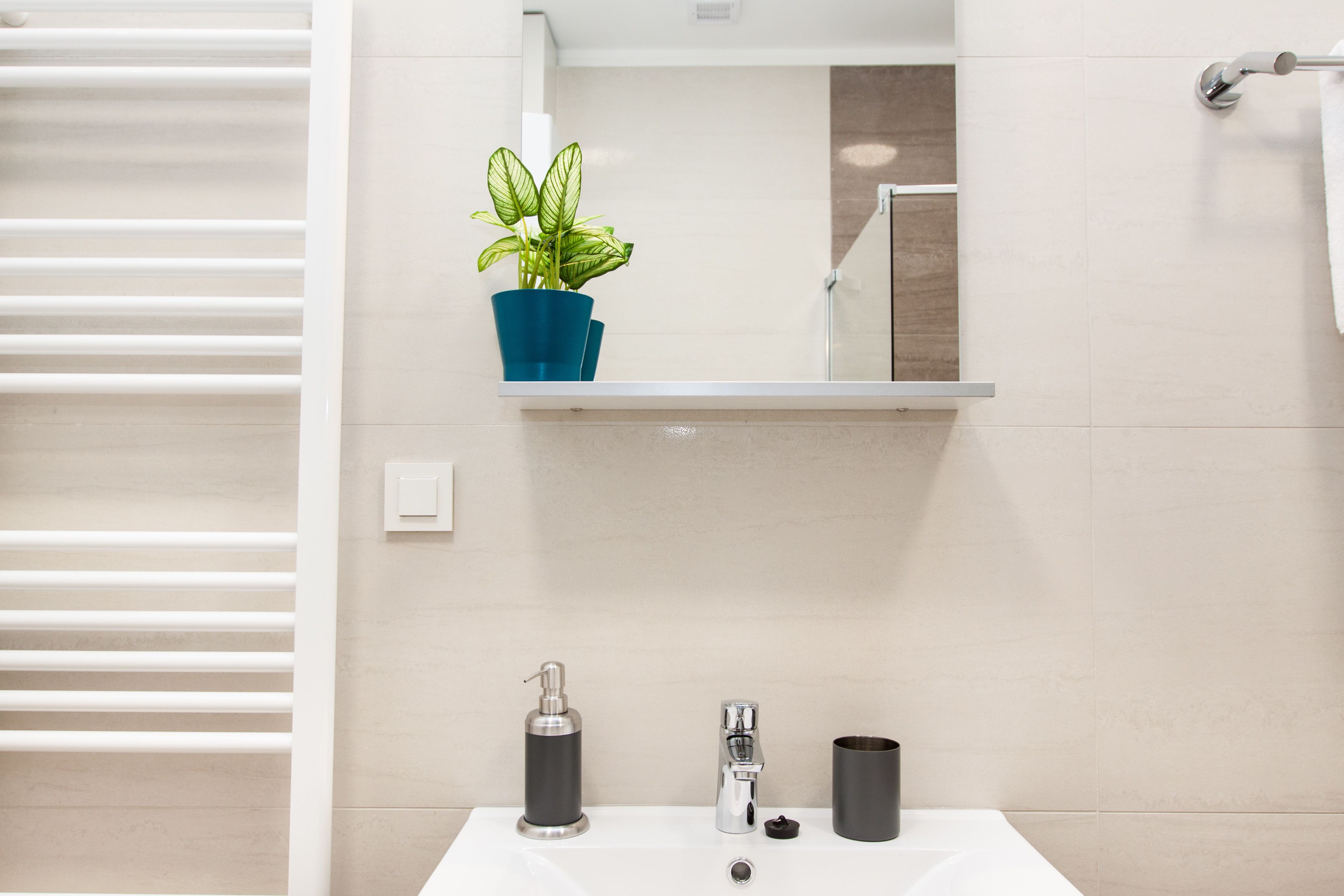 A bathroom with a white sink, a mirror above it, a potted plant, a towel rack, and a shower area.