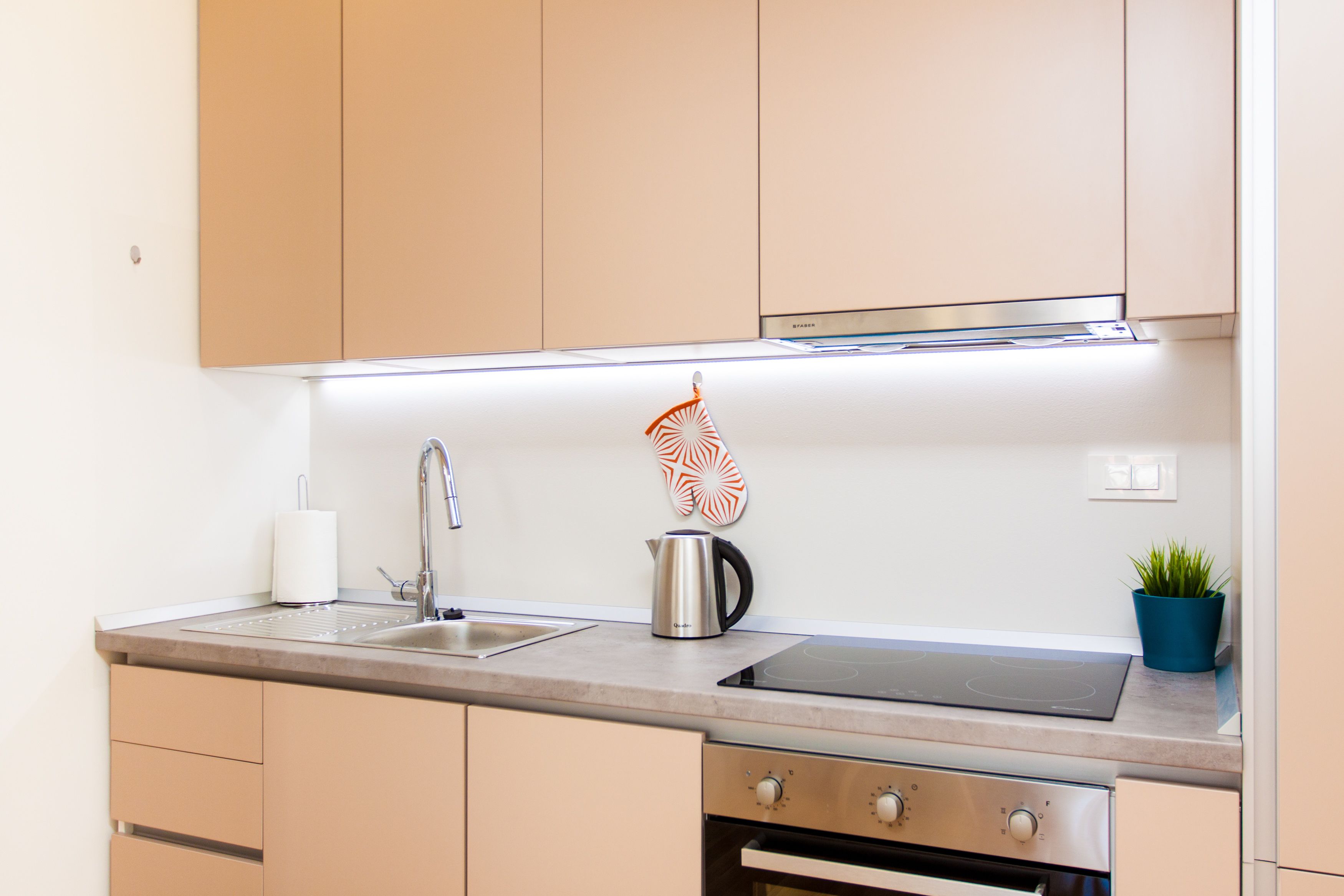 A modern kitchen with a stainless steel sink, a kettle, and a stove.