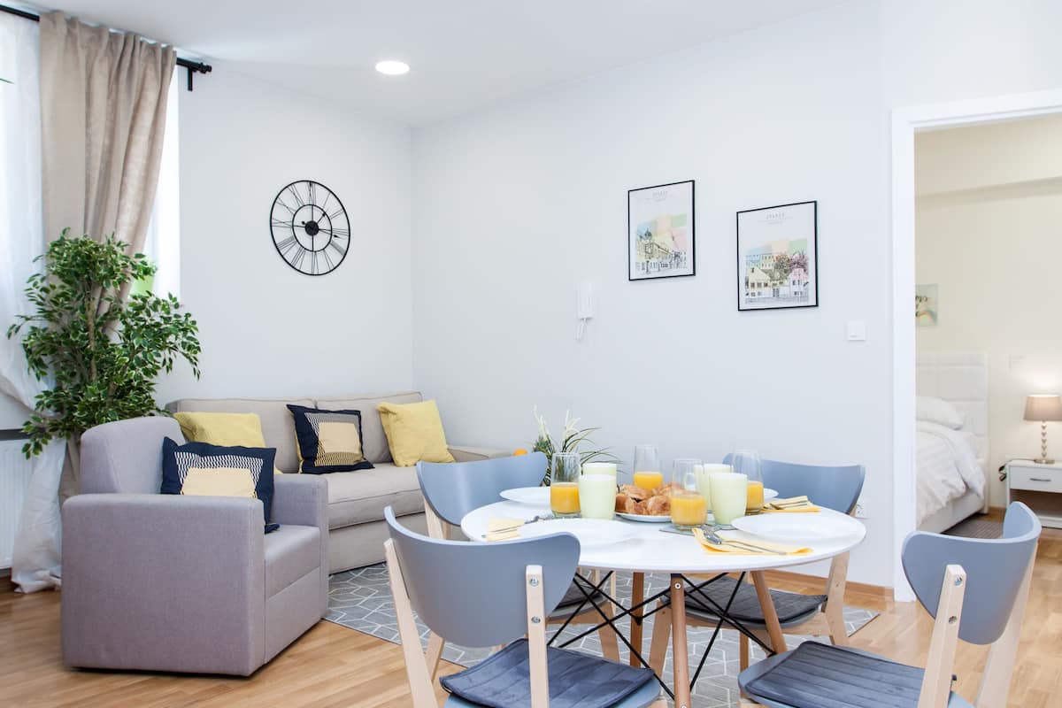 A modern living room with a dining area, a sofa set, a clock, and artwork on the walls.