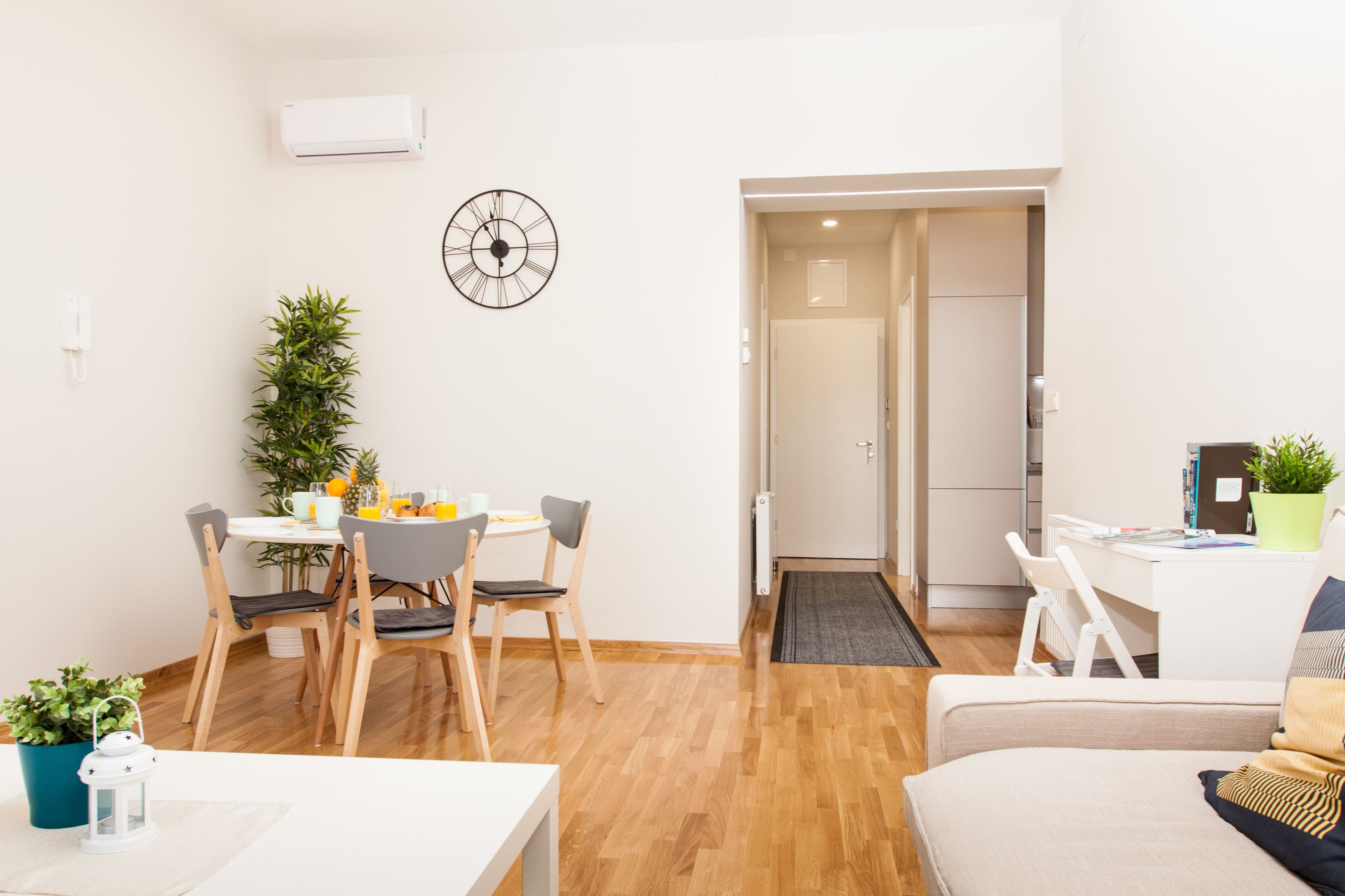 Una sala moderna con comedor, un sofá blanco, una mesa de centro y una mesita con una planta.