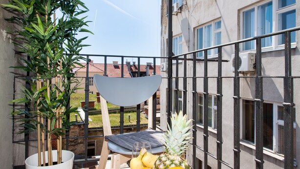 A balcony with a potted plant, a chair, and a table with fruits. - Luxury Main Square Apartments (Zagreb)