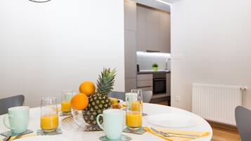 Een ontbijttafel met fruit en sapglazen, een witte tafelkleed en een moderne keuken op de achtergrond.