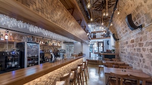 Een bar met houten toogbladen, krukken en een bakstenen muur.