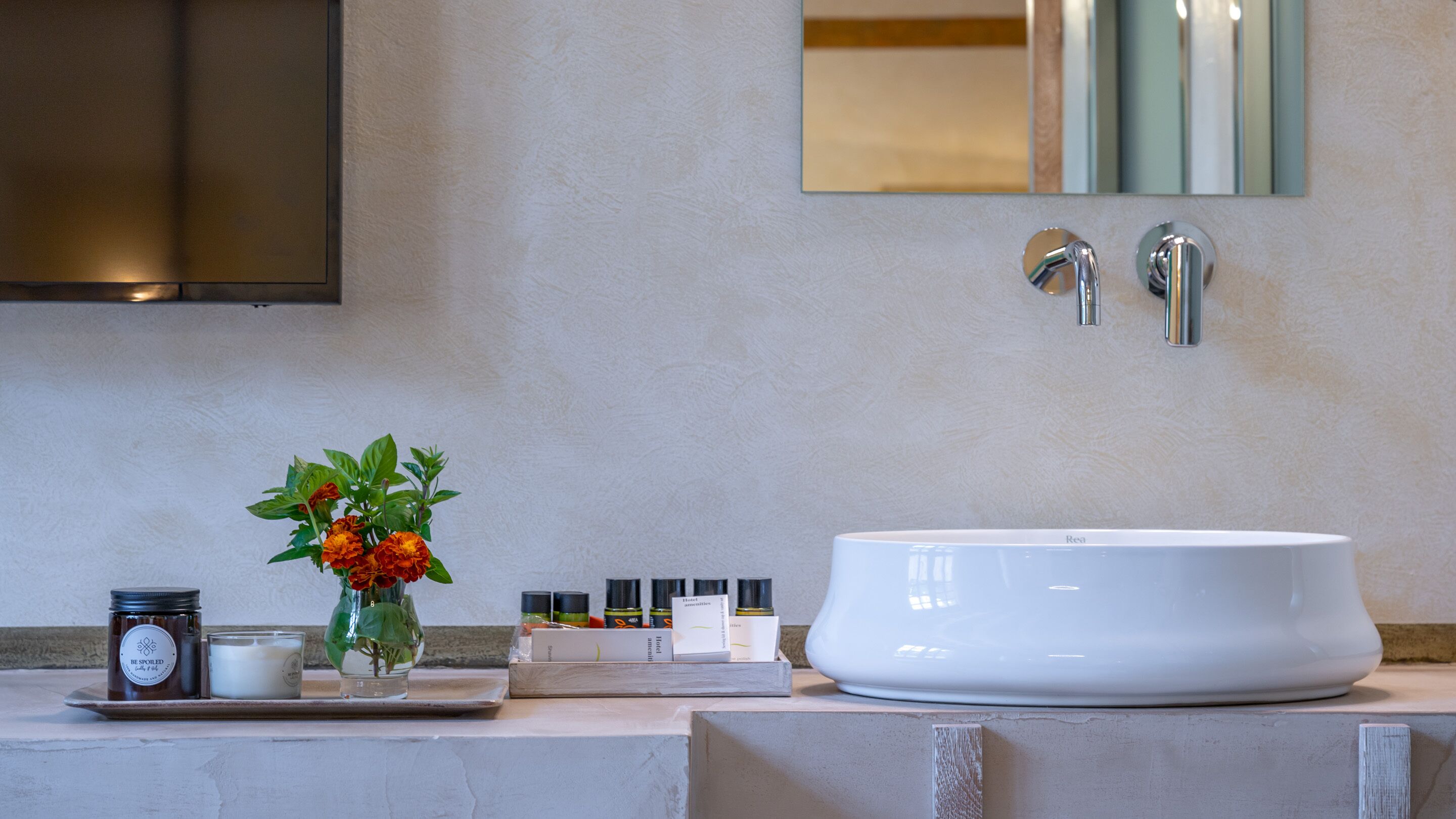 A bathroom with a large white sink, a mirror, and a small vase with flowers on the counter.