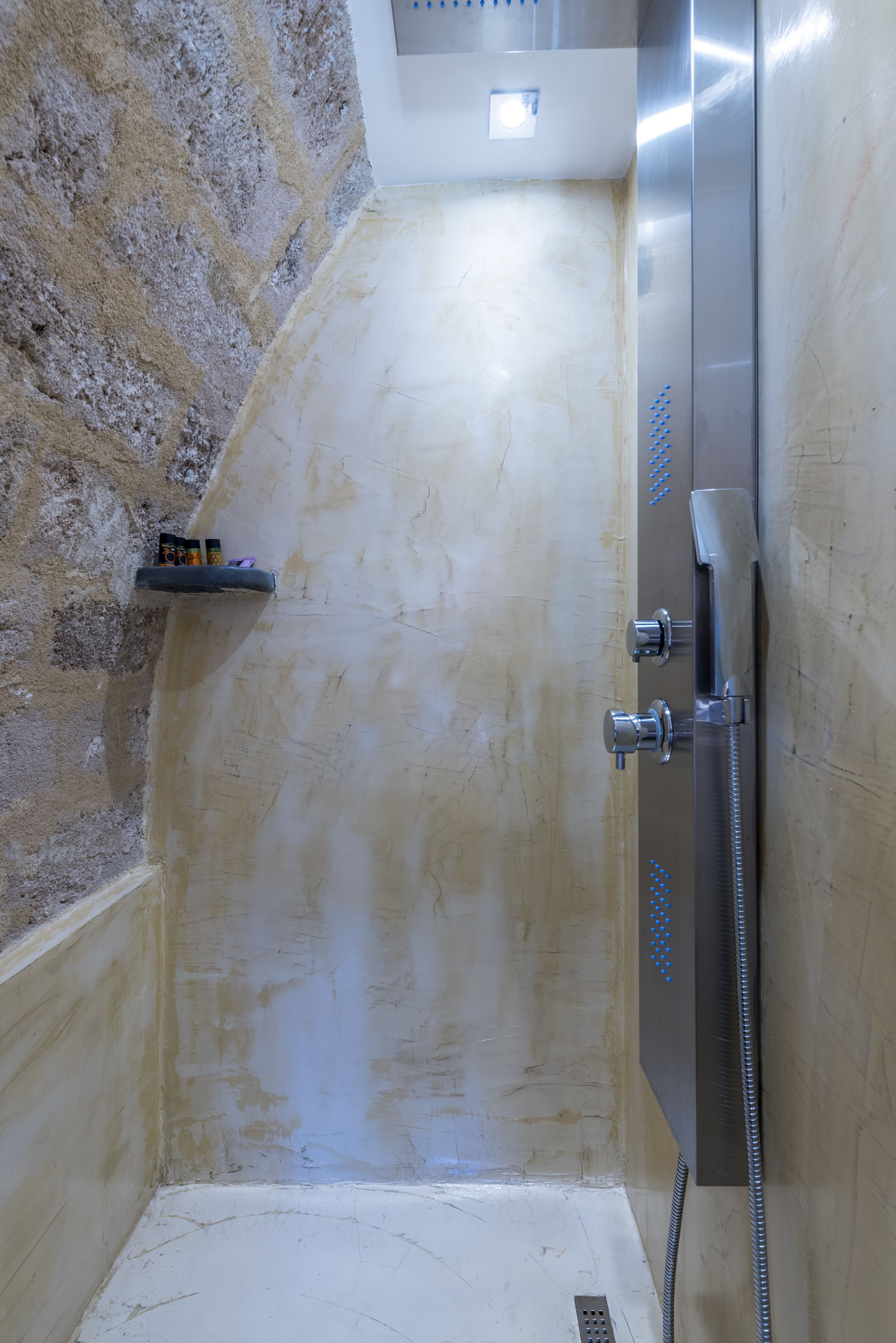 A shower with a handheld showerhead, a wall-mounted faucet, and a shelf with toiletries.