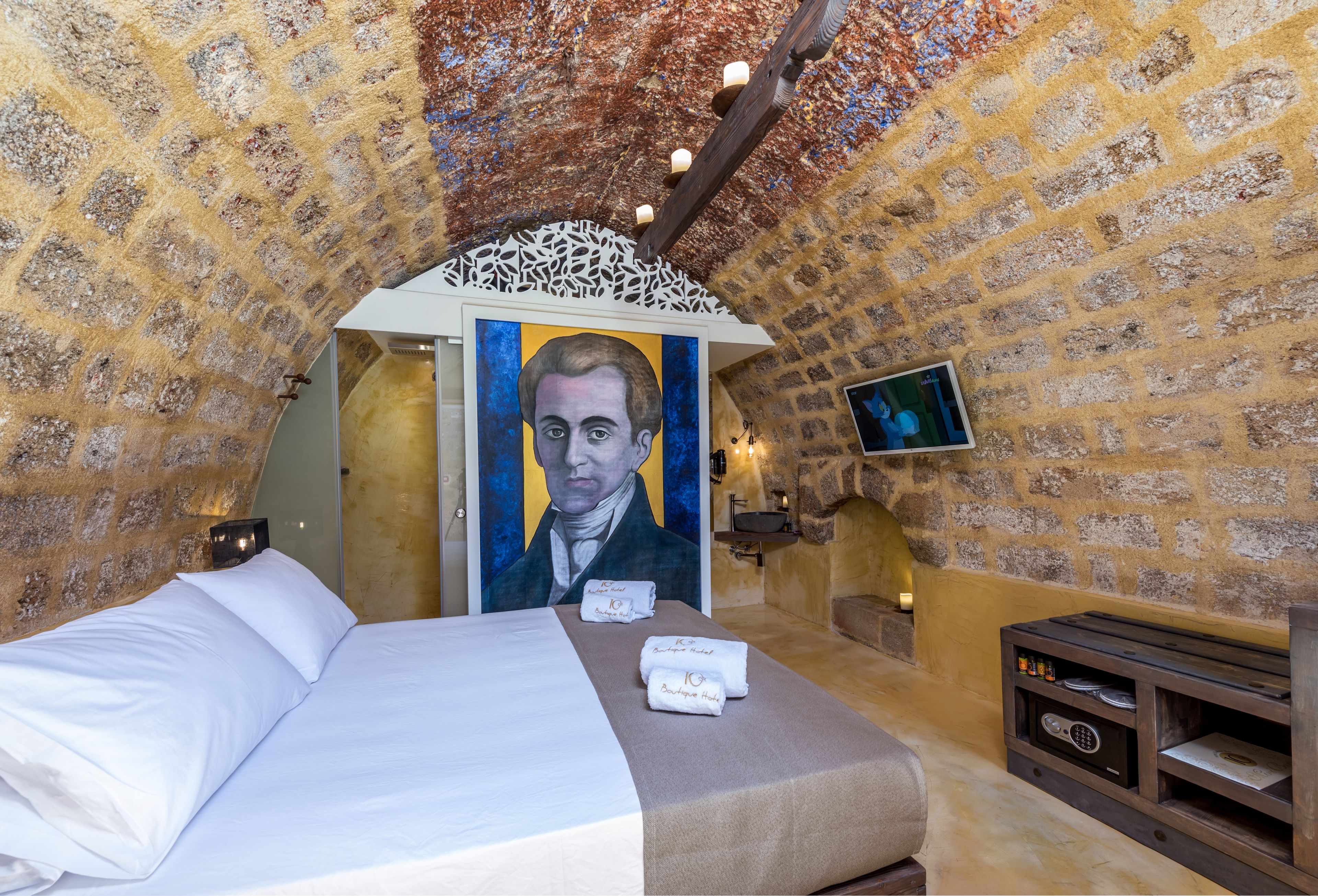 A room with a bed, a painting, a television, and a fireplace.