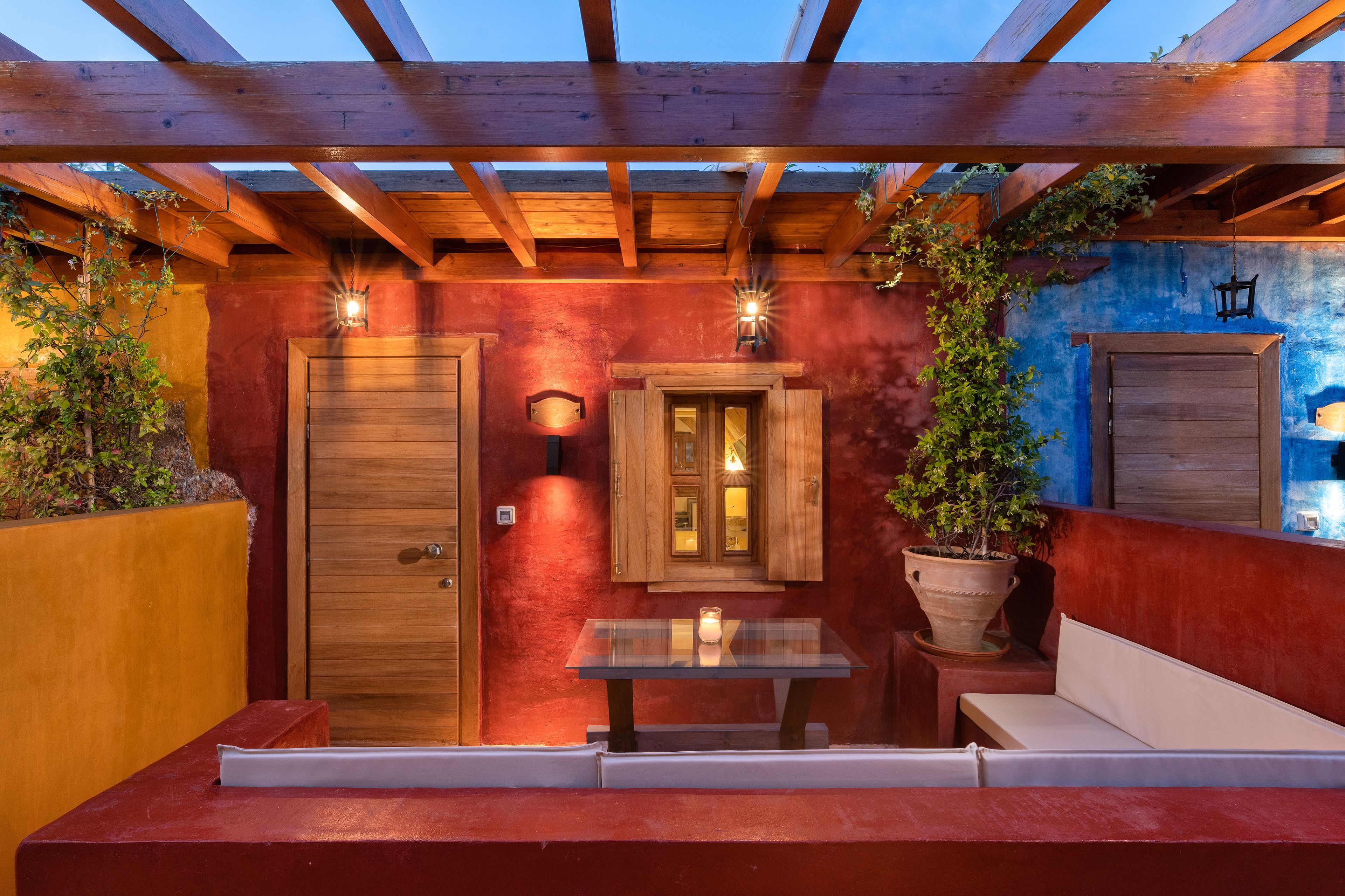 An outdoor patio with a wooden pergola, a glass table with a candle, and a bench.