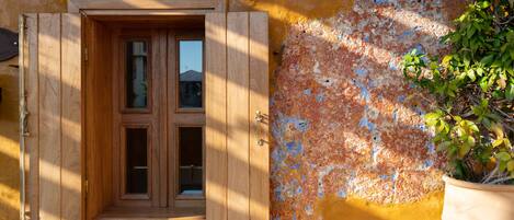 A wooden door with a window, set in a yellow wall with peeling paint.