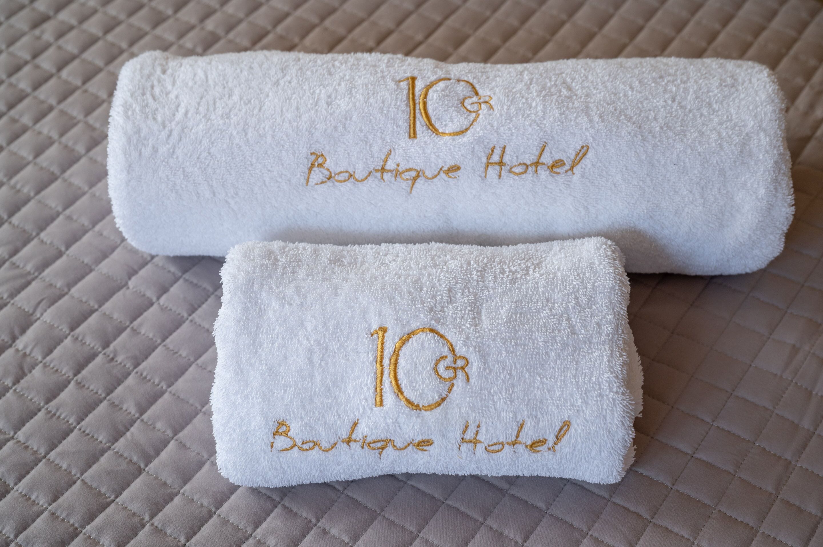 Two white towels with embroidered text "10 Boutique Hotel" on a quilted surface.