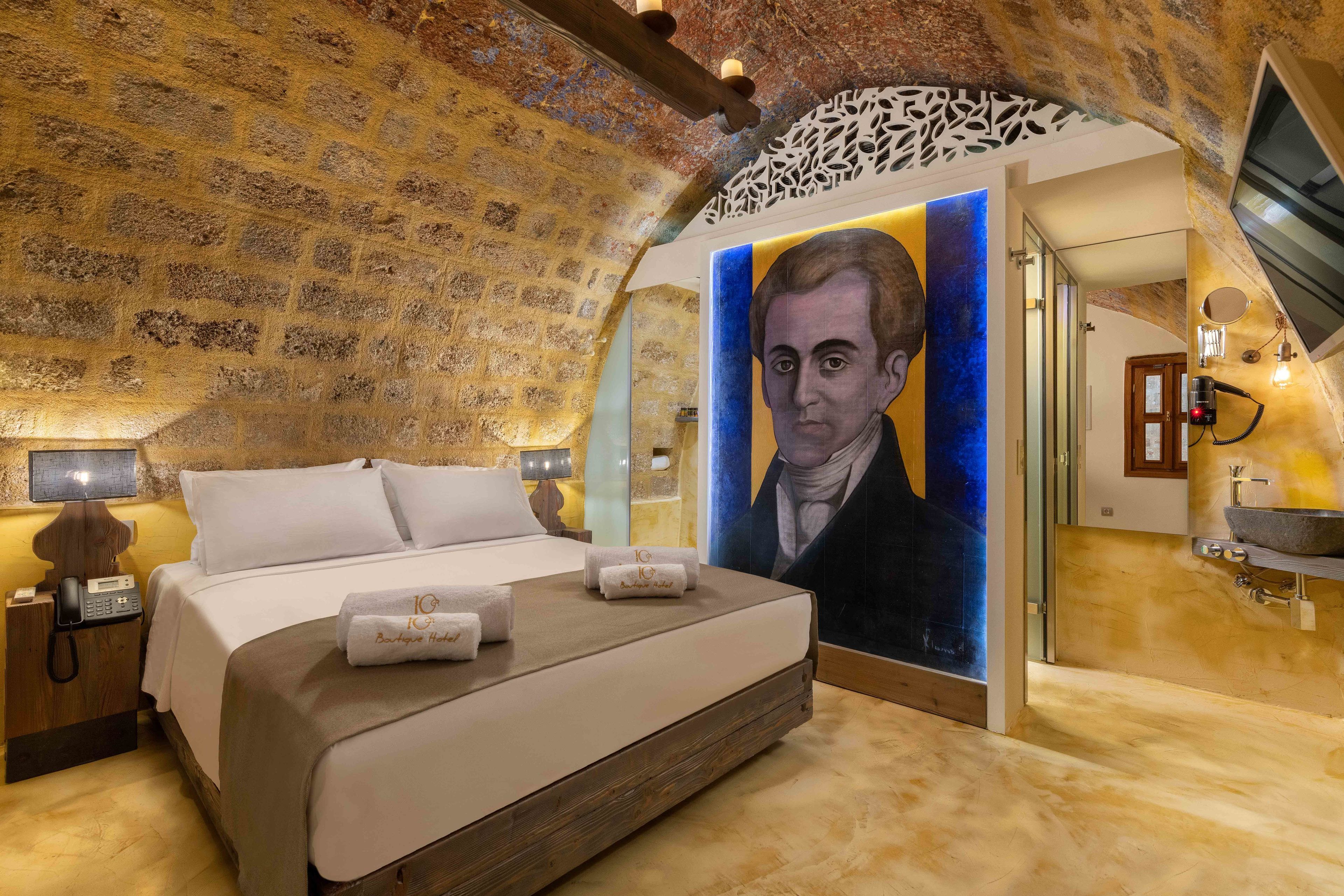Ein Schlafzimmer mit einem großen Bett, einem Wandgemälde und einem Badezimmer mit Waschbecken und Spiegel.