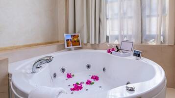 Una bañera grande y redonda con una toalla blanca, flores rosas y una pequeña mesa con un libro y un dispositivo.
