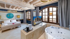 Een ruime slaapkamer met een groot bed, een badkamer met een badkuip en uitzicht op het omliggende landschap door grote ramen.
