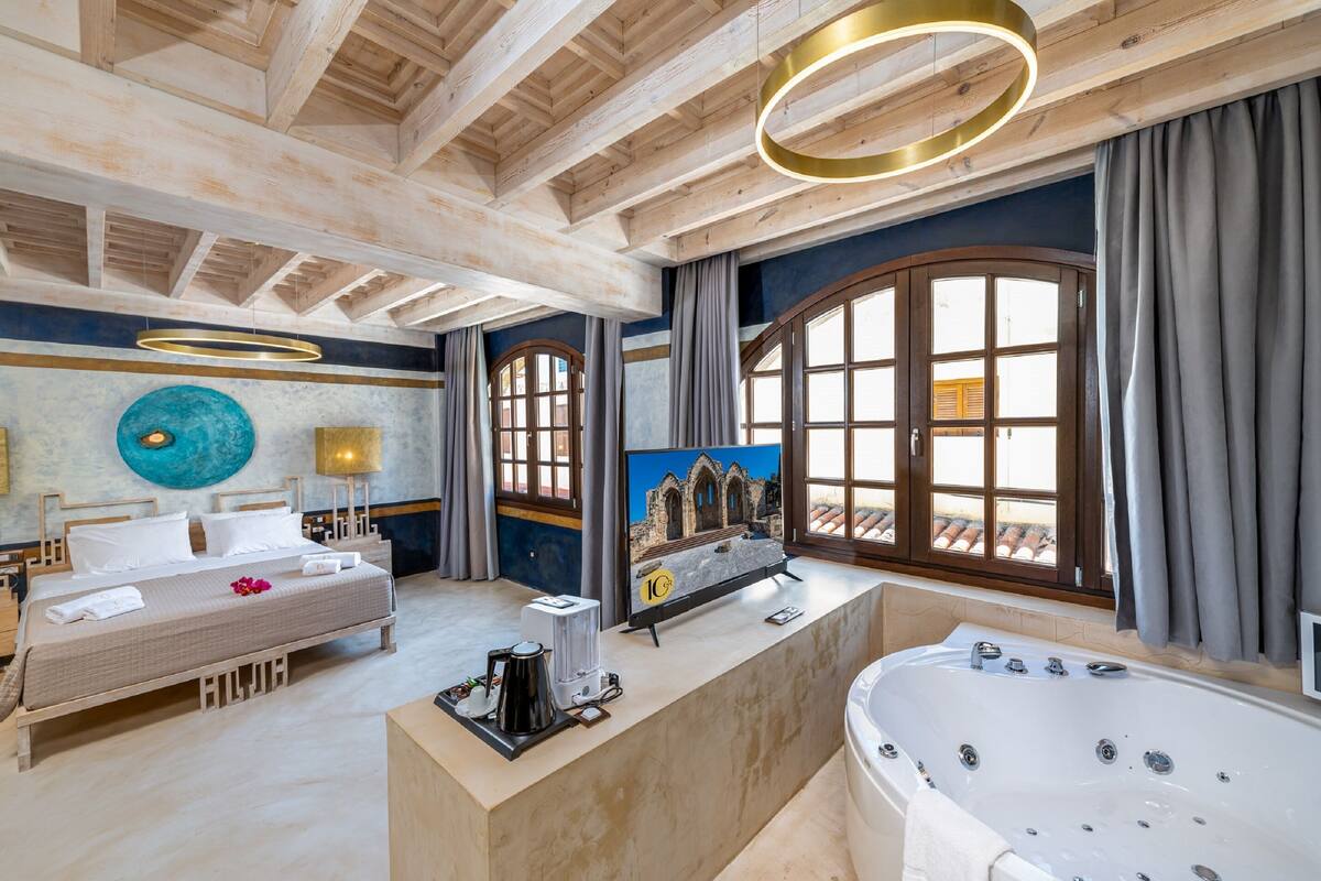 Une chambre spacieuse avec un grand lit, une salle de bain avec baignoire et une vue sur l’extérieur grâce à de grandes fenêtres.