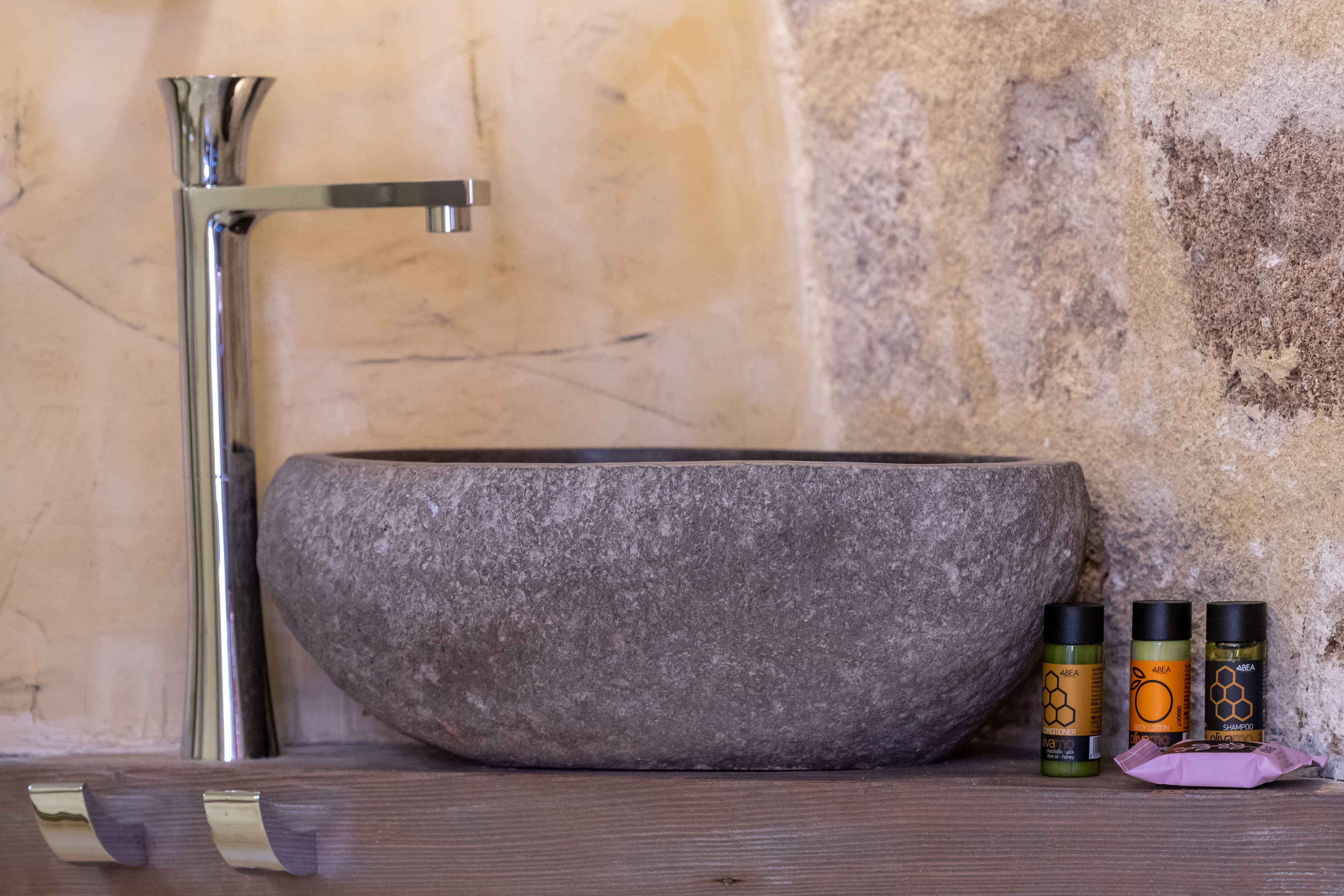 A stone basin with a faucet, next to three bottles of hair care products.