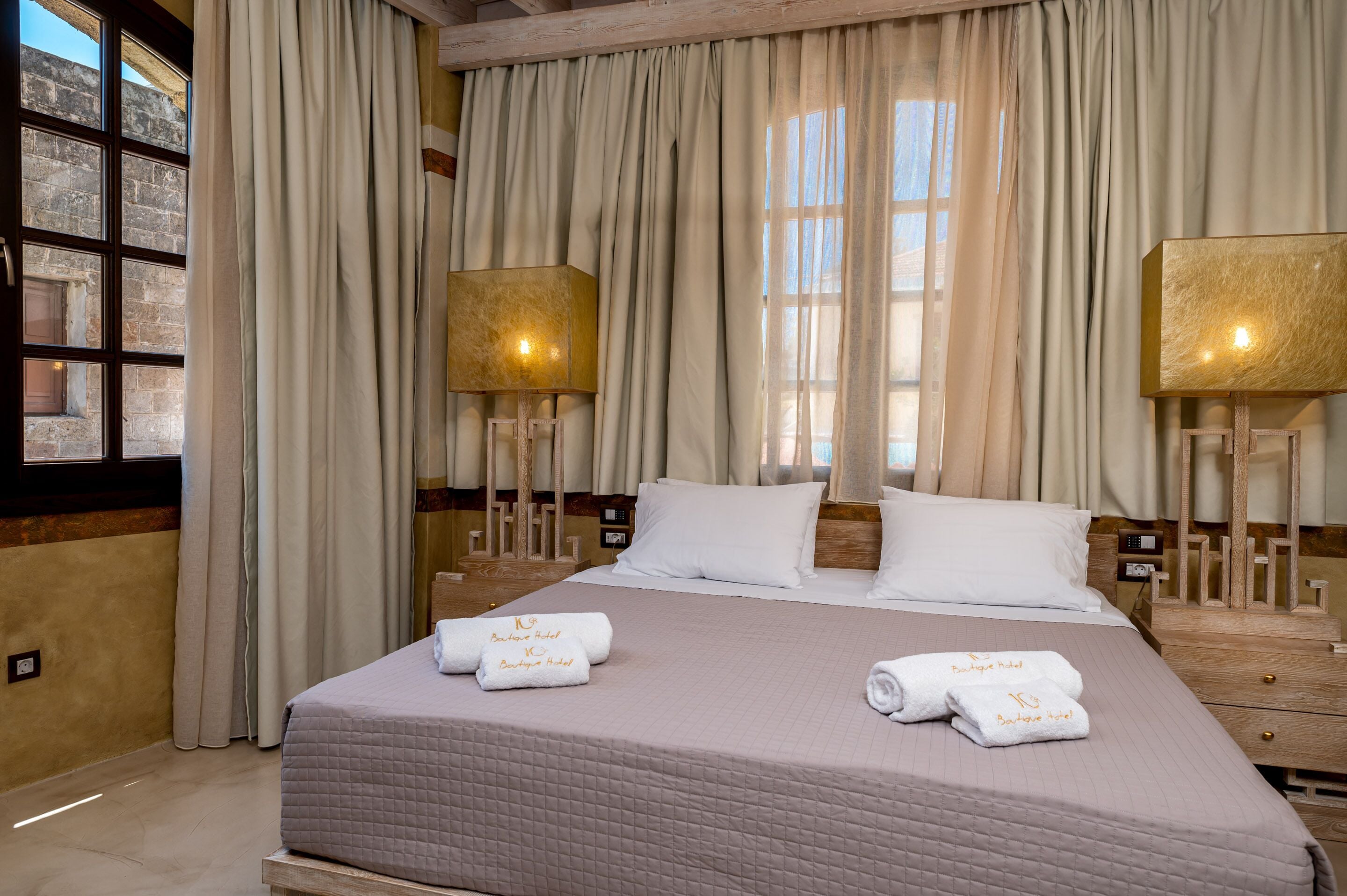 A hotel room with a large bed, two bedside lamps, and a window with curtains.