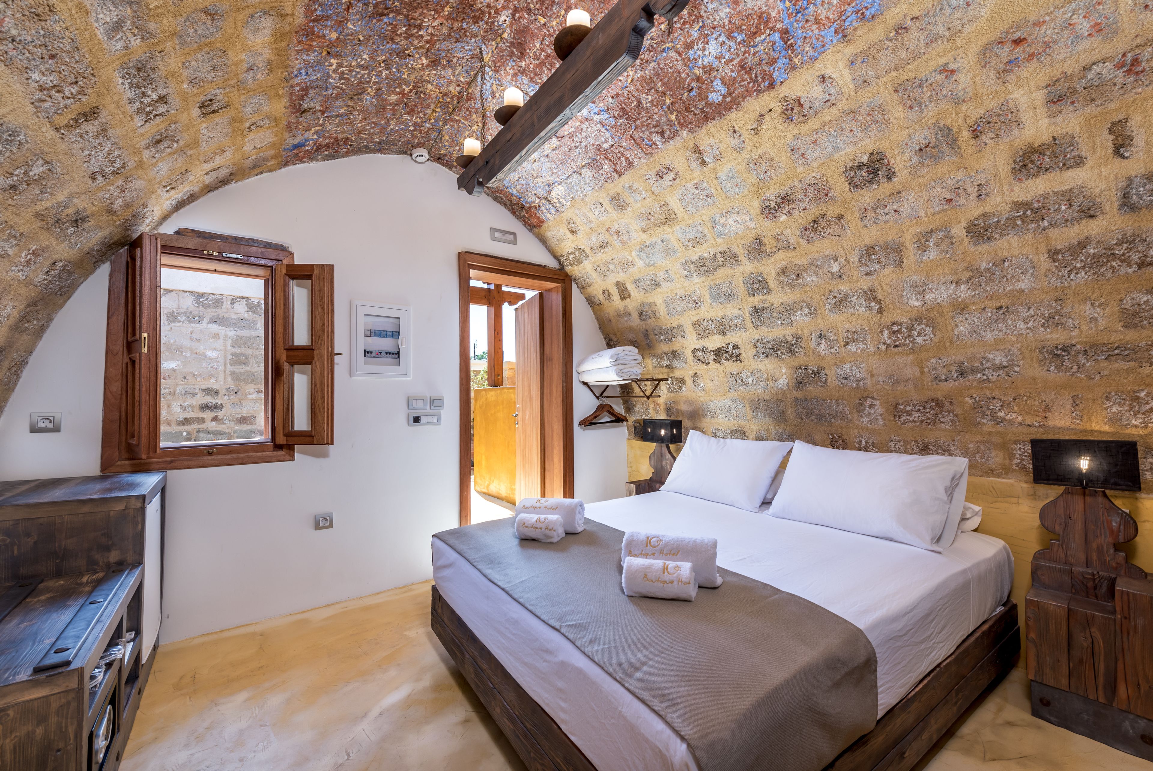 A bedroom with a stone wall, wooden beams, a bed with white linens, and a wooden dresser.