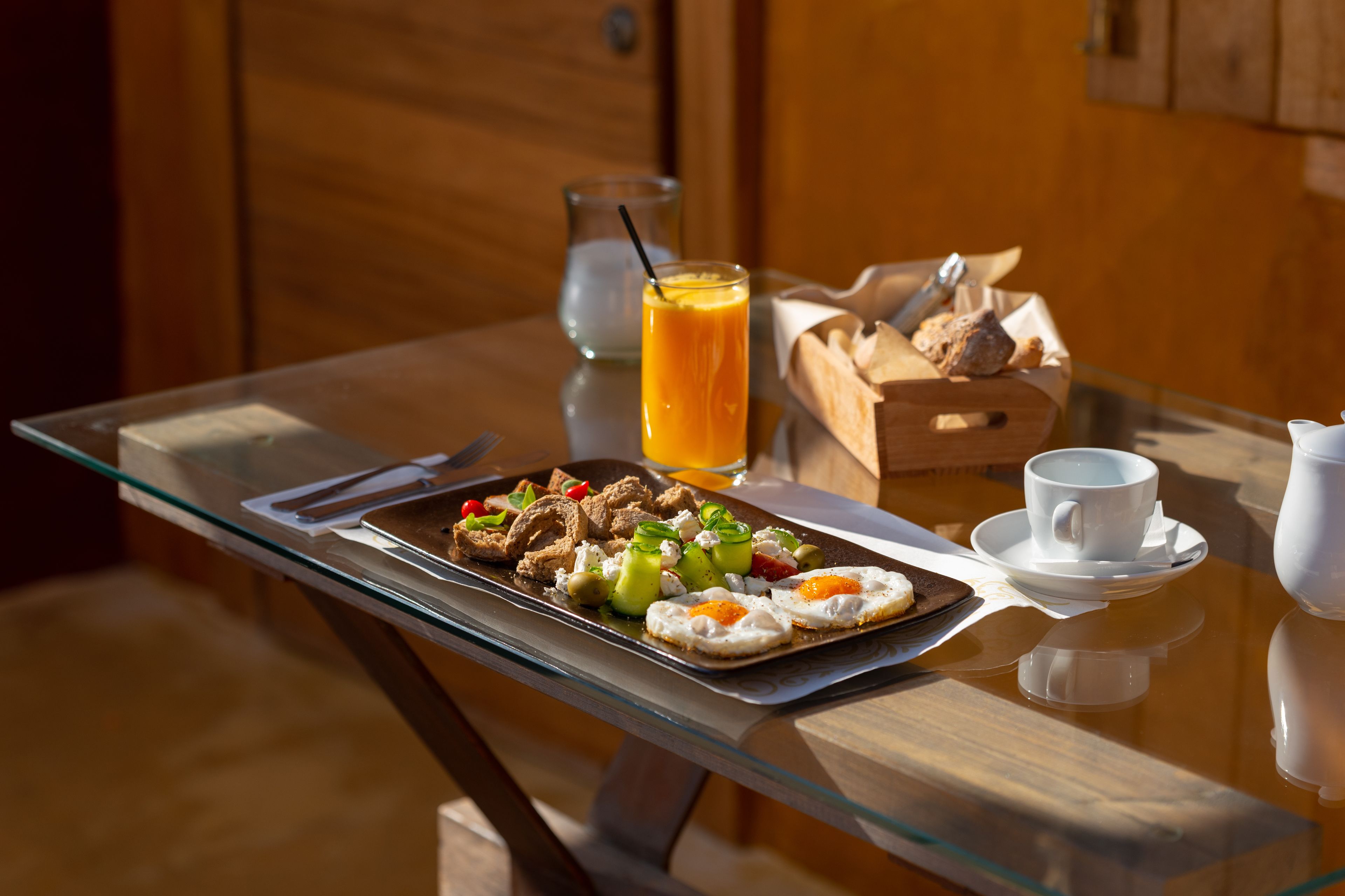 A breakfast tray with eggs, vegetables, and bread on a glass table.