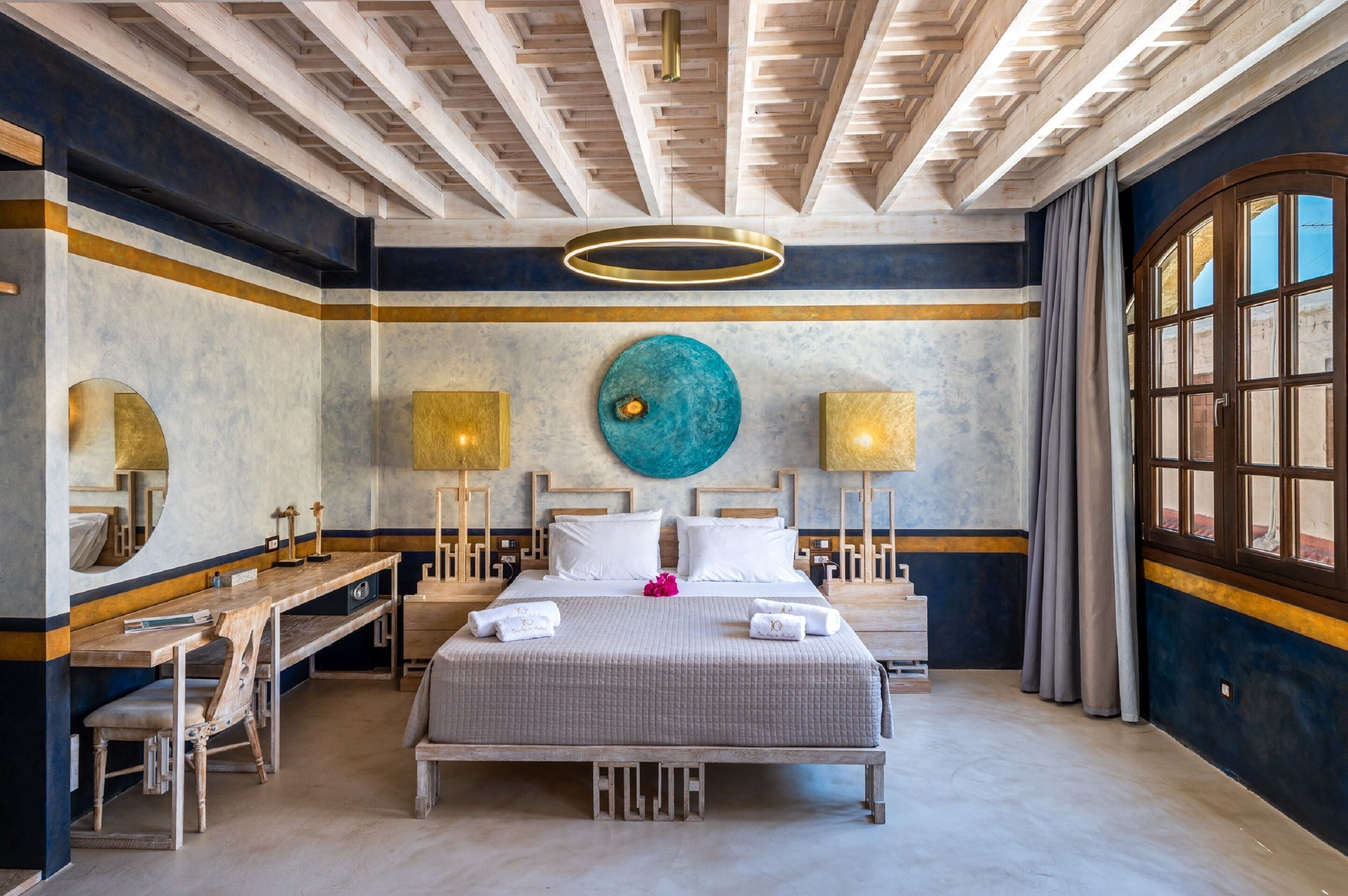 A hotel room with a large bed, bedside tables, a desk, and a large window.