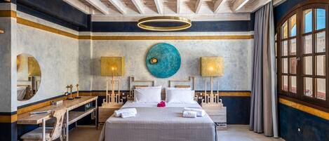 Habitación de hotel con una cama grande, mesitas de noche, un escritorio y un ventanal amplio.